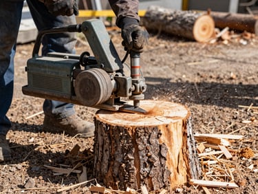 An industrial stump grinder machine carving a thick tree stump down to the soil, sharp focus on flying wood debris.
