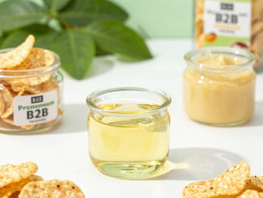 Golden vegetable oil and pure ghee in clear glass containers, surrounded by premium B2B snack foods, crisp daylight, 50mm