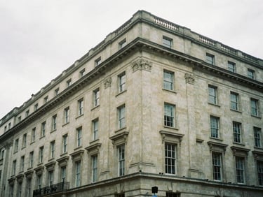 Wide architectural angle of a classic Portland stone facade on Oxford Street, overcast London sky, soft low-contrast diffused daylight, moody editorial photography, 35mm film grain.