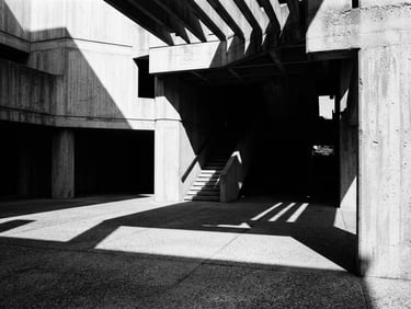 Stark monochrome architectural photography of a brutalist concrete pavilion, harsh directional light casting sharp geometric shadows across empty space, high contrast chiaroscuro.