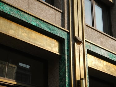 Macro architectural detail of polished brass accents and emerald-hued stone trim on a modern Art Deco building, sharp geometric shadows, sunlit.