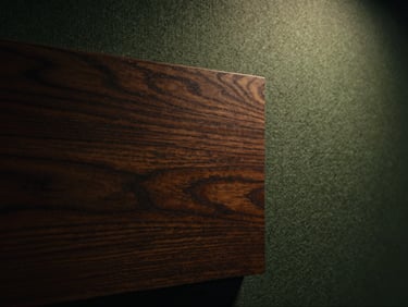 Macro close-up of dark stained walnut wood grain meeting textured acoustic fabric, warm dramatic side lighting, high contrast chiaroscuro, cinematic 35mm rendering