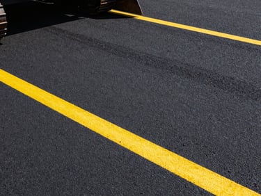 Crisp detail of freshly sealed black asphalt with bright, clean yellow parking lines, high-contrast daylight, sharp industrial photography.