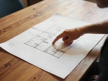 Warm candid photo of a community organizer pointing at architectural blueprints on a wooden table, soft daylight, 35mm film aesthetic
