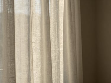Softly draped sheer linen curtains filtering warm afternoon sun, casting elegant shadows on a neutral wall.