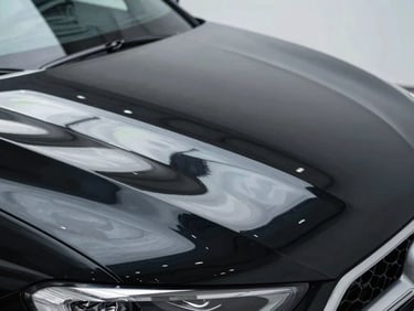 Close-up of the same black car hood after multi-stage paint correction, deep mirror-like gloss reflecting a clean overhead light perfectly, premium automotive photography