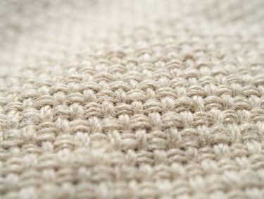 Close-up texture of pure cream-colored woven linen fabric, bright natural daylight highlighting the organic fibers, shallow depth of field, sharp focus on the textile weave.