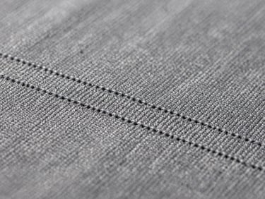 Macro close-up of precise, tight embroidery stitching on heavy slate gray cotton fabric, showing the rich weave and clean thread lines under studio light.