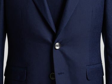Close-up of a premium navy blue executive blazer, focusing on the custom-engraved metallic button and clean lapel stitching, soft directional studio lighting.