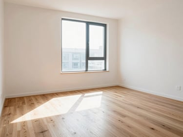 A clean, modern apartment interior with sunlight streaming through a window, showing pristine hardwood floors.