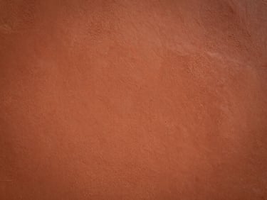 Close-up of warm terracotta wall texture with raking side light, deep ochre and burnt sienna tones, rough plaster surface, editorial still, no people