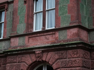 Architectural detail of a carved stone facade of a historic estate, soft, diffused light, emphasizing heritage and integrity. Editorial heritage photography, soft natural window light, muted deep crimson and forest green tones, 35mm, shallow depth of field.