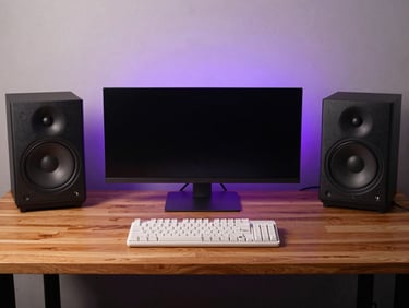 Symmetrical wide shot of a clean desk setup with warm wood tabletop, dual studio monitors, white mechanical keyboard, and a soft purple glow on the back wall
