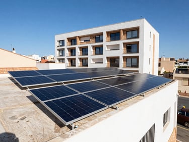 Vista en ángulo de paneles solares instalados sobre la cubierta plana de un edificio residencial moderno en Alicante, cielo azul despejado, luz solar directa brillante.