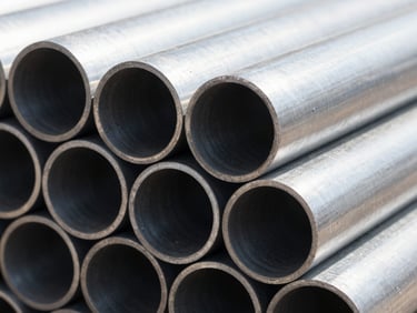 Close-up macro photography of stacked industrial steel pipe profiles, bright natural daylight highlighting metallic circular edges, high contrast, 35mm lens.