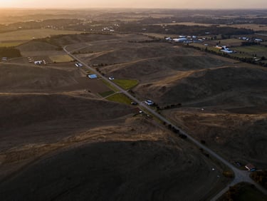Sweeping aerial drone shot of raw rolling land lots and strategic development parcels at dusk, warm low-contrast light
