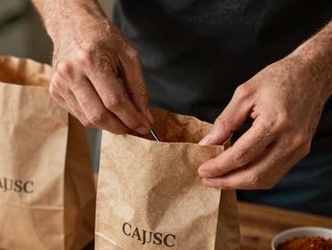 Hands carefully packing signature Cajun spice blends into brown paper bags, warm ambient lighting.
