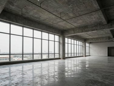 Completed commercial office floor in Jaipur — open-plan concrete ceiling with exposed services, polished floor reflecting diffused overcast daylight from floor-to-ceiling windows, structural grid clearly legible, no occupants, material documentation framing