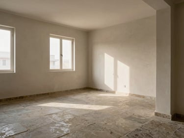 Finished residential apartment interior, Jaipur — living area with stone-finish flooring, plastered walls under soft north-facing window light, structural column visible in corner, no furniture staging, material quality foregrounded