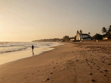 Wide coastal panorama of a Goa beach at golden hour, a lone figure walking along the tide line at the far left, Portuguese colonial church facade visible at right middle distance, warm amber sky, long shadows across the sand