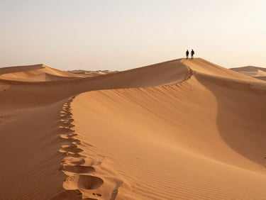 Sweeping panoramic view of Jaisalmer desert dunes at early morning, two travelers as tiny silhouettes climbing a dune ridge at the upper right, vast orange sand sea filling the frame, pale dawn sky, long raking shadows across dune faces