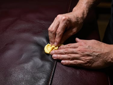 Hands applying wax to a thick black leather seam, moody workshop lighting, rich textures, 85mm lens