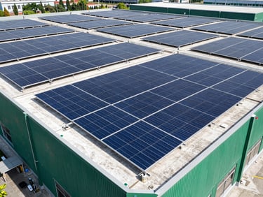 Wide architectural shot of a large commercial building with a vast, clean solar array on its rooftop, bright daylight, sharp shadows.