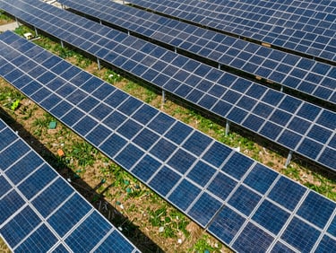Aerial view of a modern commercial solar array with power lines, bright daylight, sharp shadows, deep blue and emerald tones, wide-angle lens, high-end commercial aesthetic