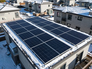Drone shot of a residential rooftop solar array partially covered in light snow, highlighting clean design, bright daylight, sharp shadows, deep blue and emerald tones, wide-angle lens, high-end commercial aesthetic