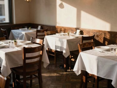 Interior of a small artisanal restaurant, empty tables set for service, warm late-afternoon window light casting long shadows across wooden chairs and white linens, intimate and unhurried