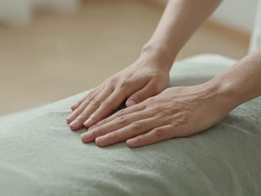 Close-up of hands gently hovering over a clothed client, soft morning light casting gentle shadows, warm sand and muted sage tones, shallow depth of field, 35mm.