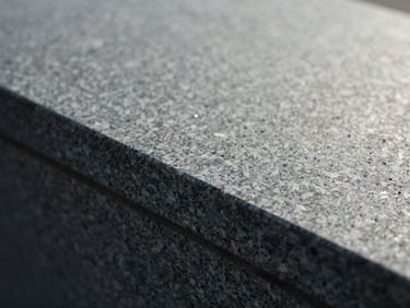 Macro detail shot of dark gray granite texture catching soft morning sun, showing deep crystalline grain, 35mm film texture