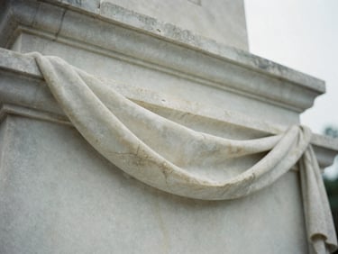 Close-up of finished carved marble drapery detail on a monument, soft overcast light, muted stone tones, shallow depth of field