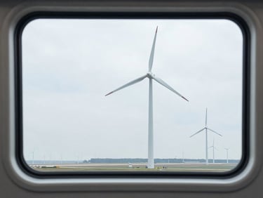 Scenic view of modern wind turbines and a distant runway framed perfectly through a clean, double-paned train window, cool overcast daylight, sharp focus.