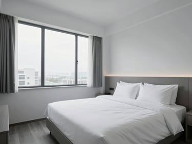An empty, pristine hotel room with crisp white linens and clean architectural lines, cool daylight streaming through a large window.