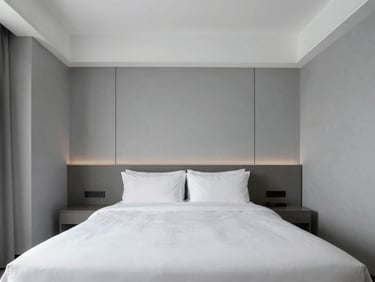 An empty luxury hotel room with crisp white linens, minimalist slate grey walls, symmetrical architectural framing, cool daylight.