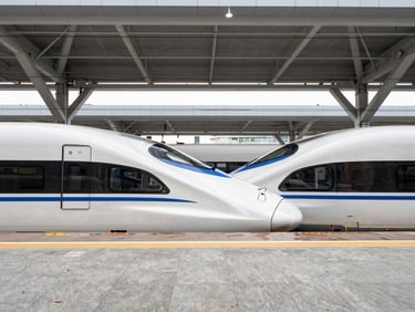 Symmetrical architectural shot of a high-speed train waiting at a modern concrete platform under a geometric steel canopy, crisp daylight, sharp focus.