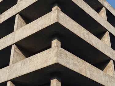 Tight abstract crop of a concrete building corner, architectural geometry, strong shadows, crisp natural daylight, deep navy and warm amber tones.