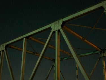 Abstract structural geometry of a steel bridge truss against a dark evening sky, low-key lighting, deep emerald tones