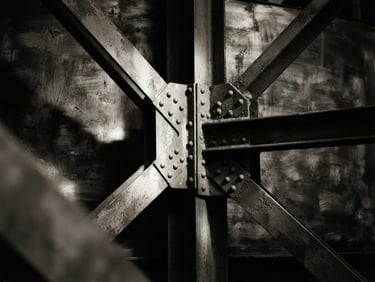 Monochrome close-up of structural steel intersections, dramatic side lighting with deep shadows, textured brush background, desaturated warm tones, medium format film