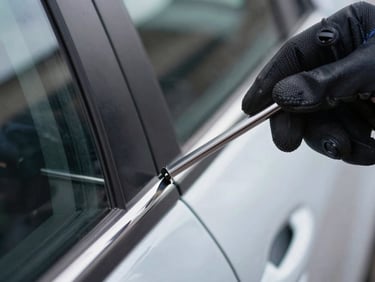 Extreme close-up of a technician's gloved hand inserting a slim jim tool into a car door frame, cool daylight, sharp focus on tool edge and door rubber seal