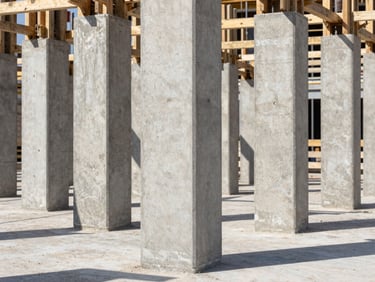 Detailed shot of reinforced concrete structural pillars on a clean construction site in Bologna, straight-on architectural angle, bright daylight, crisp shadows.
