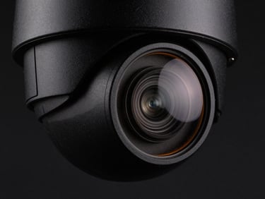 Macro shot of a high-end dome security camera, matte black casing, subtle amber rim light reflecting off the glass lens, dark moody studio lighting, technical aesthetic.