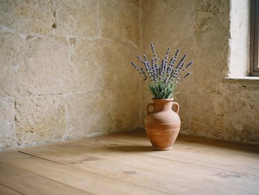 A simple wooden floor in a sunlit room with ancient stone walls, a single terracotta vase with wild lavender in the corner, soft focus.