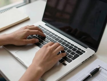 Close-up of hands typing a business proposal document on a laptop, overhead natural window light, clean desk surface with a notebook and pen in frame corner