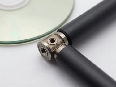 Extreme close-up overhead of a PEEK disc and PA-CF rod on white ground, studio-bright even light showing precise layer lines and matte surface finish, 1-2cm depth of field