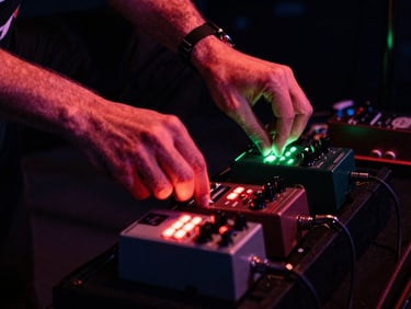 Close-up of a guitarist's hands adjusting analog effects pedals on a dark stage, glowing red and green LED lights, high-contrast, grainy.