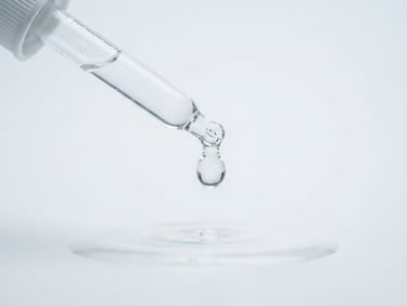 Crisp macro product photography of clear liquid drops dispensing from a glass pipette, bright cool studio light, clinical white backdrop, 100mm macro lens