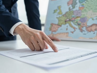 Close-up of a hand pointing to a section of a business plan document on a desk, with a blurred map of Europe in the background, cool natural daylight.