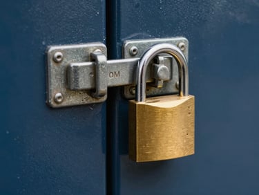 Close-up shot of a heavy-duty brass padlock securing a steel latch on a clean navy metal storage door, bright and even lighting.